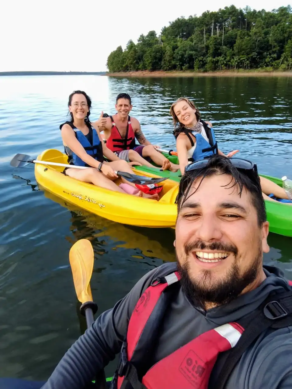 A group in double kayaks on the lake, smiling at the camera.