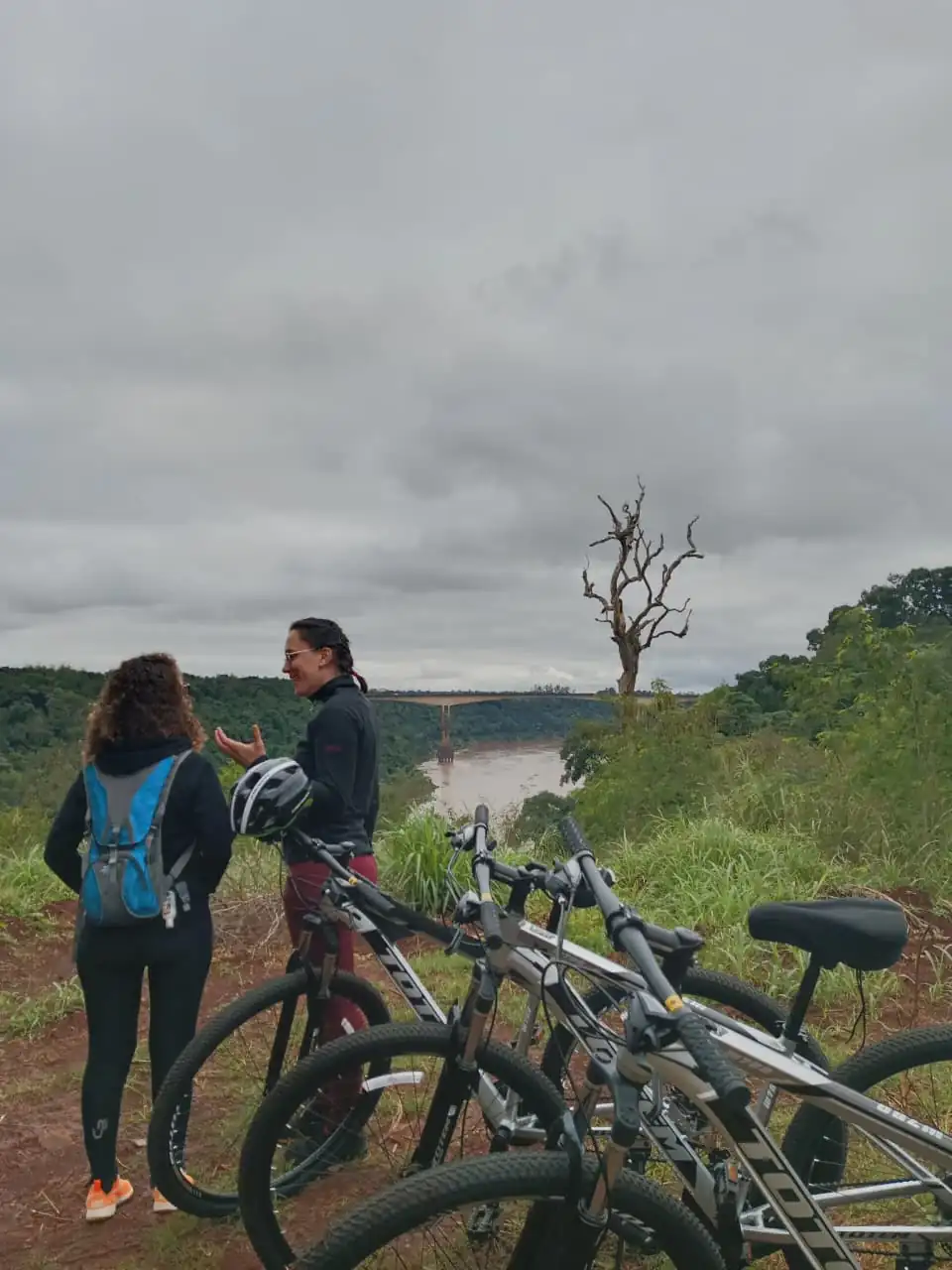 Dos ciclistas se detienen en un mirador sobre el río, con las bicis apoyadas.