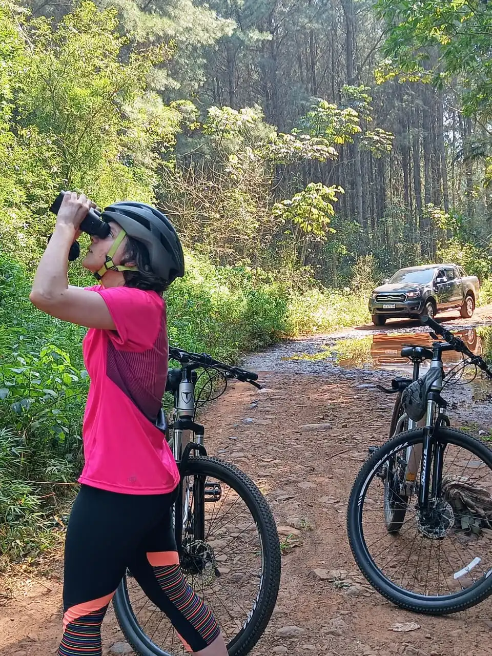 Una ciclista se detiene a mirar con binoculares, con las bicis apoyadas al costado.